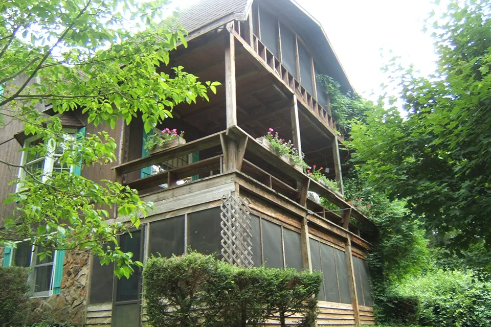 Wooden house with screened porch and green foliage.