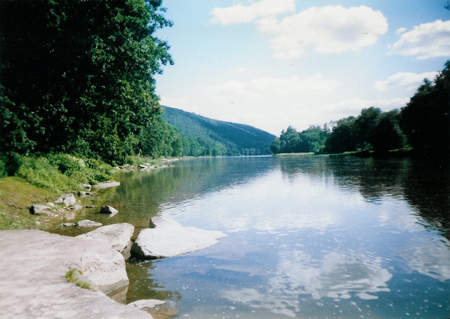 A calm river reflecting clouds and trees.